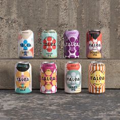 six cans of various flavored sodas lined up against a concrete wall with the word talga on them