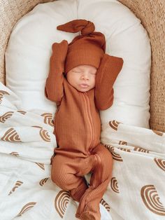 a baby in a brown outfit laying on top of a bed