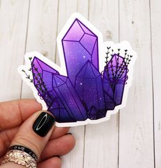 a hand holding a purple sticker with crystals on it