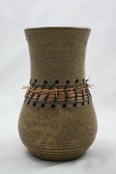 a brown vase with some black dots on the rim and handles, sitting on a white surface