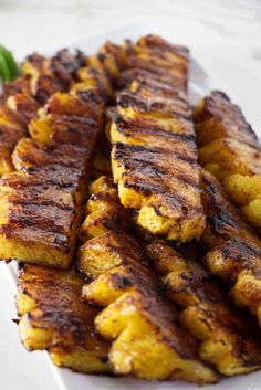 grilled bananas on a white plate with some green garnish in the background