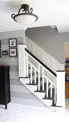 the stairs in this house are painted gray and white with striped walls, framed pictures on either side