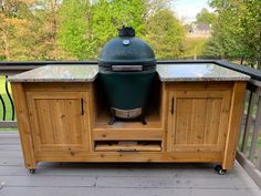 a big green egg sitting on top of a wooden table next to a grill area