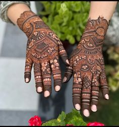 two hands with henna designs on them, one is holding a potted plant