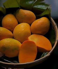 a basket filled with lots of oranges on top of a wooden table next to green leaves