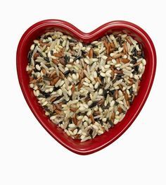 a red heart shaped bowl filled with nuts and seeds on top of a white background