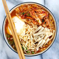 a bowl of noodles, meat and vegetables with chopsticks on a marble surface