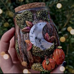 a hand holding a glass jar decorated with fall leaves and moon on it's side