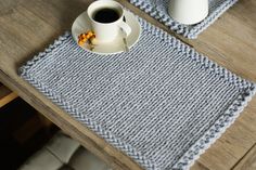 a cup of coffee sits on a table next to a knitted placemat and mug