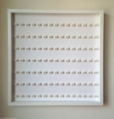 a white framed art piece with lots of small beads on it's sides, hanging on the wall