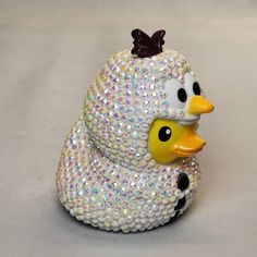 a white and yellow rubber duck with sequins on it's head