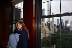 a woman standing in front of a window looking out at the city