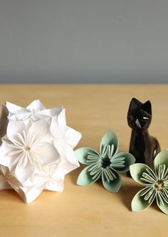 three paper flowers sitting on top of a wooden table next to a cat figurine