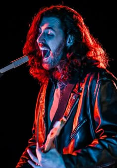 a man with long hair and beard singing into a microphone while wearing a leather jacket