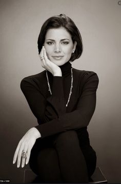 a black and white photo of a woman with her hand on her chin, sitting down