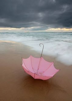 an umbrella sitting on top of a sandy beach next to the ocean under a cloudy sky