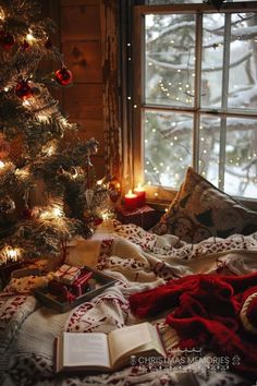 a christmas tree in front of a window with lights and blankets on the bed next to it