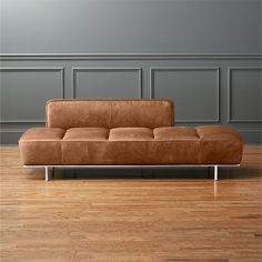 a brown couch sitting on top of a hard wood floor next to a gray wall