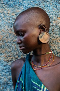 a woman with earrings on her head standing in front of a stone wall