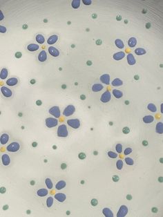 a white plate with blue and yellow flowers on it's rim, in the center is green dots