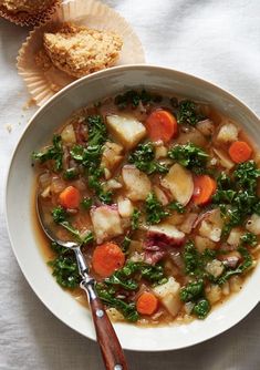 a bowl of soup with carrots, kale and bread on the table next to it