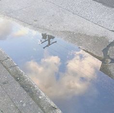 a reflection of the sky and clouds in a puddle