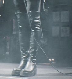 a woman in black leather boots is holding a microphone and standing on stage with her legs crossed