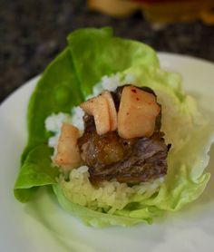 a white plate topped with lettuce and meat covered in sauce on top of rice