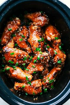 a slow cooker filled with chicken wings covered in sesame seeds and garnished with green onions