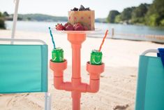 there is a cake and two cups on the table in the sand by the water