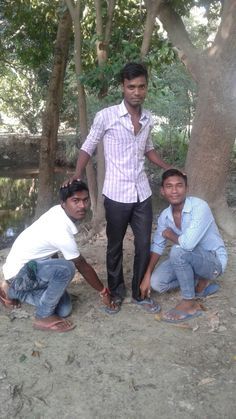 three men are posing for the camera in front of some trees and dirt, while one man is holding his hand out