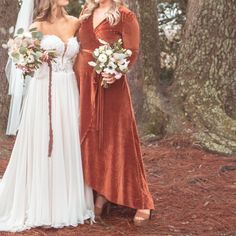 two women standing next to each other in the woods wearing dresses and holding bouquets