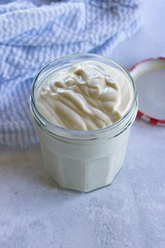 a glass jar filled with cream sitting on top of a white counter next to a blue towel