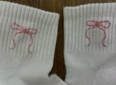 two pairs of white socks with pink bows on them, sitting on a wooden surface