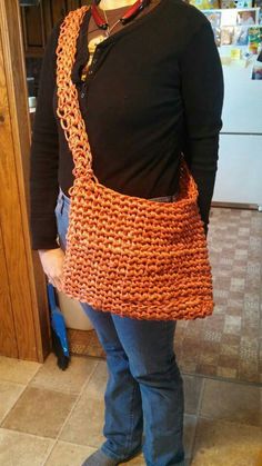 a woman wearing an orange crochet purse standing in front of a kitchen counter