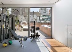 an exercise room with lots of equipment in front of a large glass window overlooking the city