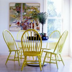 a white table with four yellow chairs and a potted plant on top of it