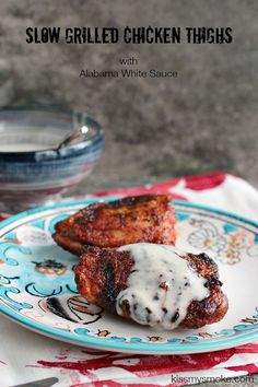 two grilled chicken thighs on a blue and white plate next to a bowl of sauce