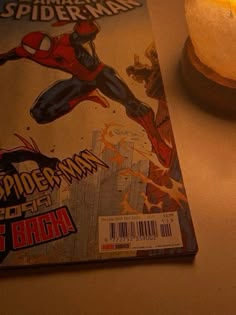 a spider - man comic sitting on top of a table next to a lit candle