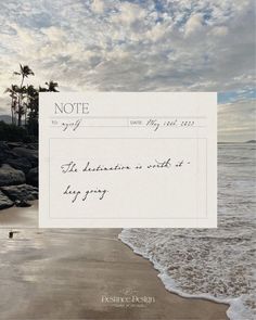 a note sitting on top of a sandy beach next to the ocean with palm trees