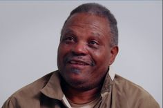 an older man wearing a brown shirt and looking at the camera with a serious look on his face