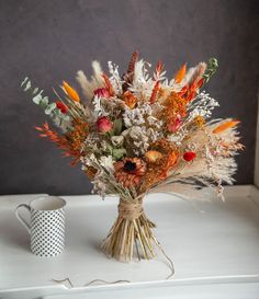 a bouquet of flowers sitting on top of a white table next to a cup and mug