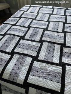 a black and white quilt on a bed with a chair in the backgroud