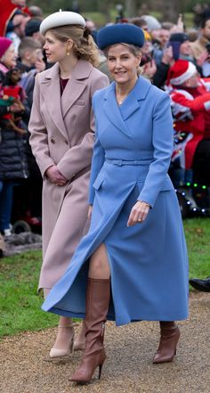 two women in blue coats and hats are walking down the street with other people behind them