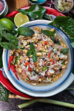 a white bowl filled with food on top of a red and blue plate next to green leaves