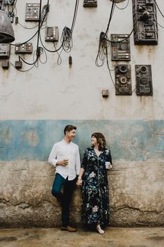 a man and woman standing next to each other in front of an old wall with telephones on it