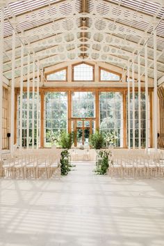 an indoor wedding venue with white chairs and greenery