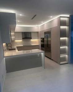 an empty kitchen with stainless steel appliances and white flooring is lit by recessed lighting