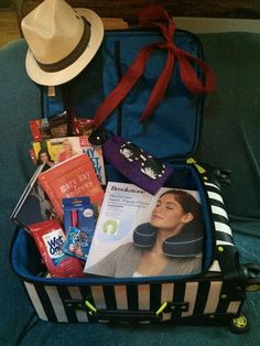 an open suitcase filled with various items on top of a blue couch next to a hat