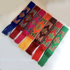 many different colors of scarves hanging on a white wall with long tassels